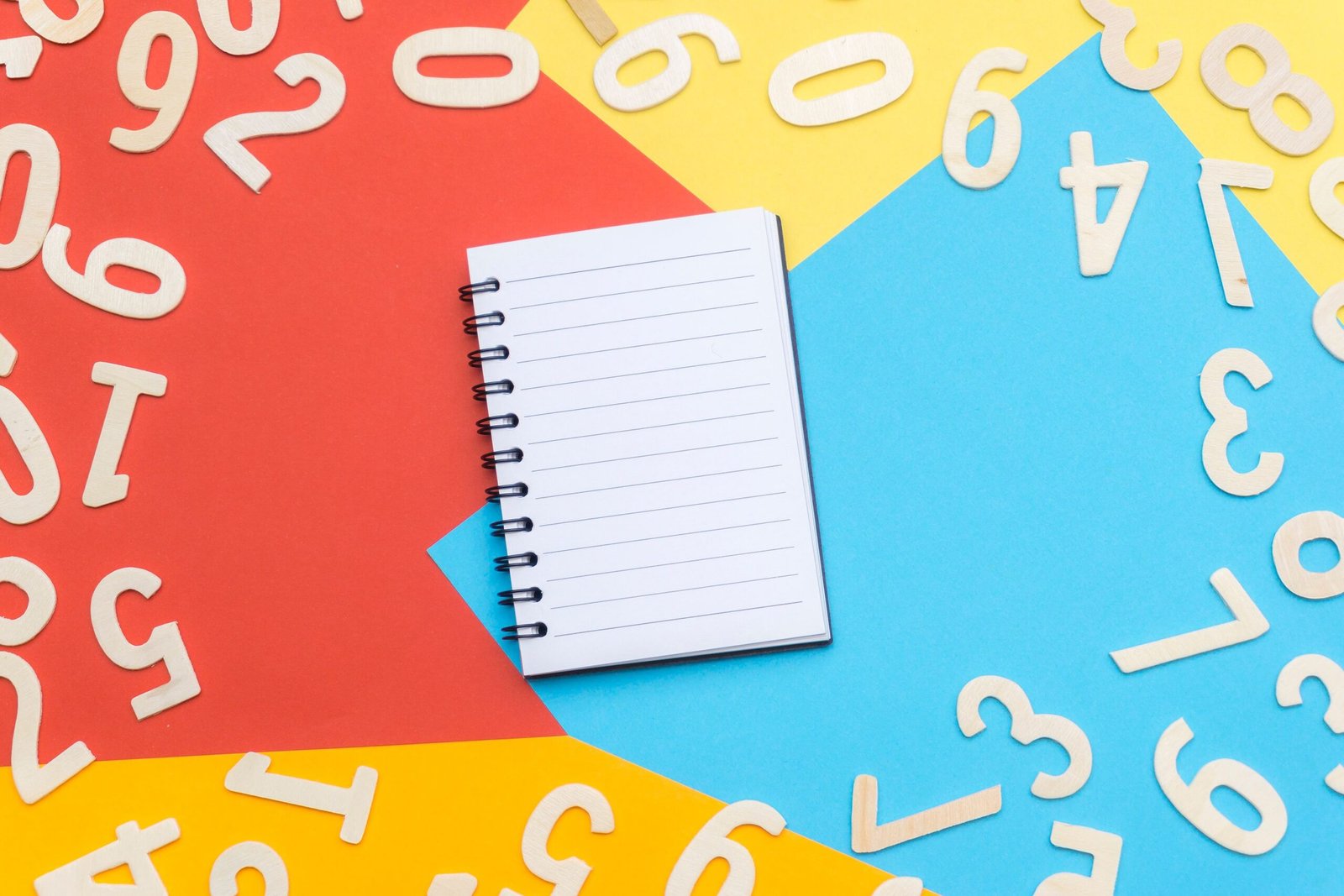 A spiral notebook surrounded by wooden numbers on a colorful geometric background, featuring red, yellow, and blue.