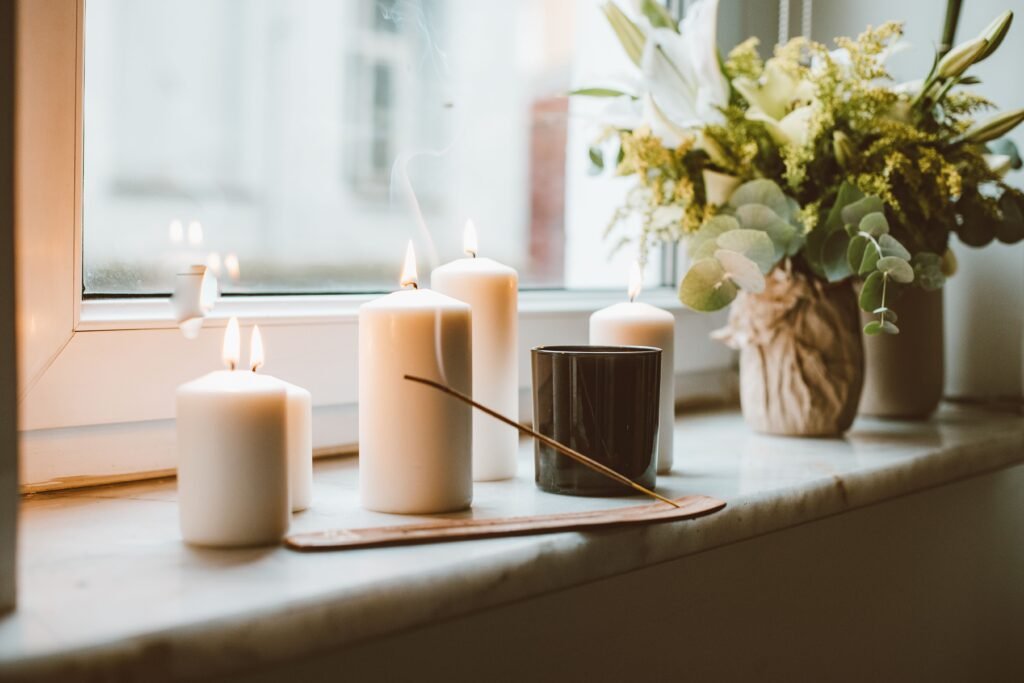 Terapias y Sesiones A serene setup of candles and flowers on a window sill, creating a calming atmosphere.