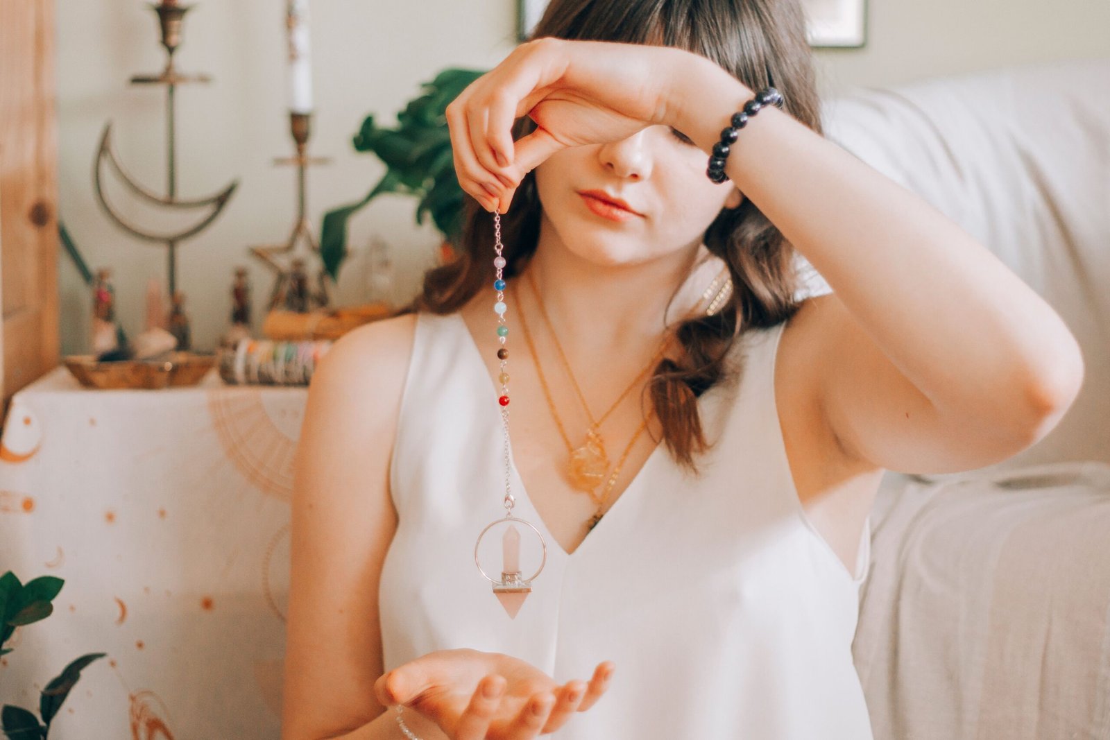 Young female with dark long wavy hair and swinging crystal pendulum over hand while soothsaying future