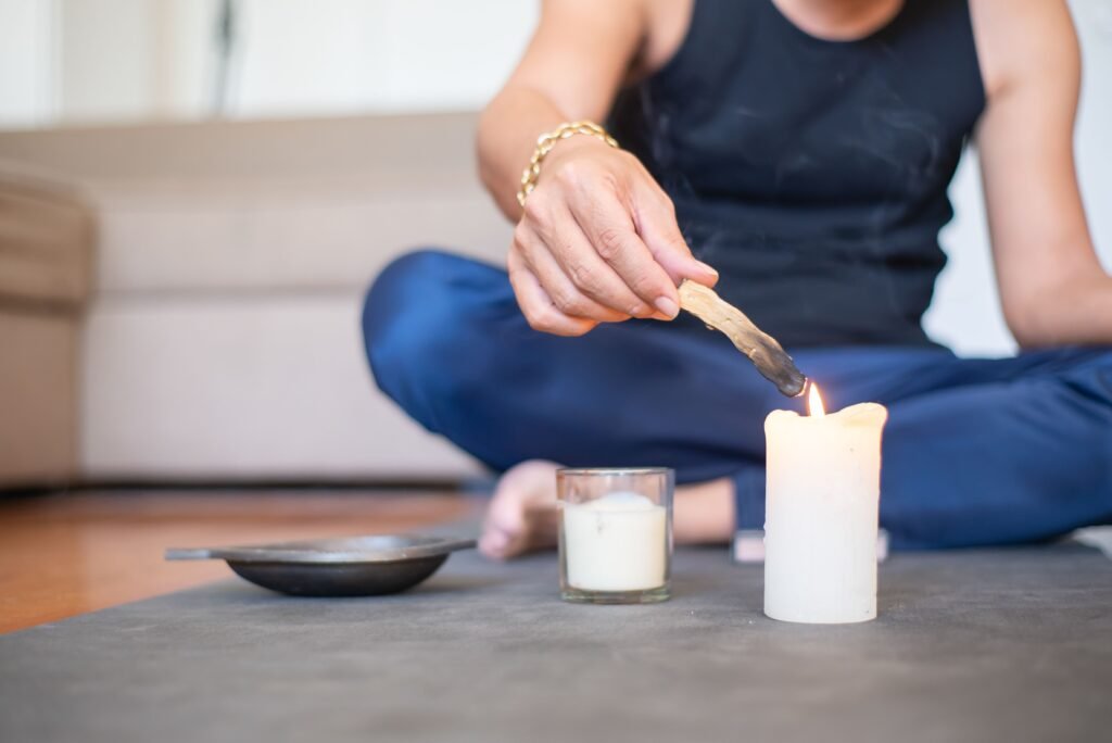 Terapias y Sesiones A man sits cross-legged indoors, lighting a candle for relaxation and meditation.
